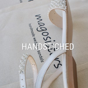 May include: White leather sandals with pearl embellishments. The sandals have a simple design with three straps and a buckle closure. The text "HANDSTITCHED" and "magosilvers" is visible on the sandals.