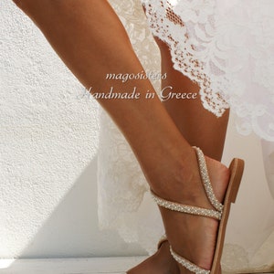 May include: Tan leather sandals with multiple straps adorned with white pearls. The sandals have a simple design and are perfect for a summer wedding or special occasion.