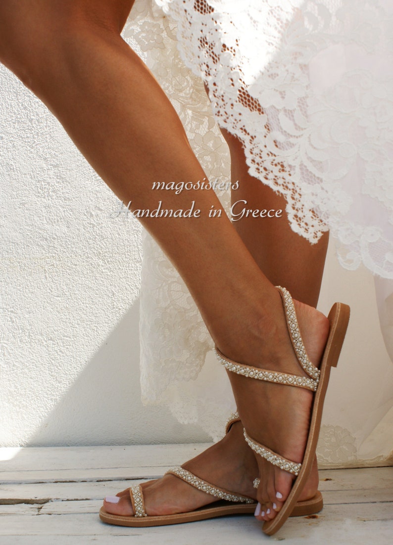 May include: Tan leather sandals with multiple straps adorned with white pearls. The sandals have a simple design and are perfect for a summer wedding or special occasion.