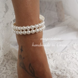 Puede incluir: Un tobillo de perlas blancas con dos filas de perlas. El tobillo est&aacute; en el tobillo de una persona y el texto "magosisters handmade in Greece" es visible debajo del tobillo.