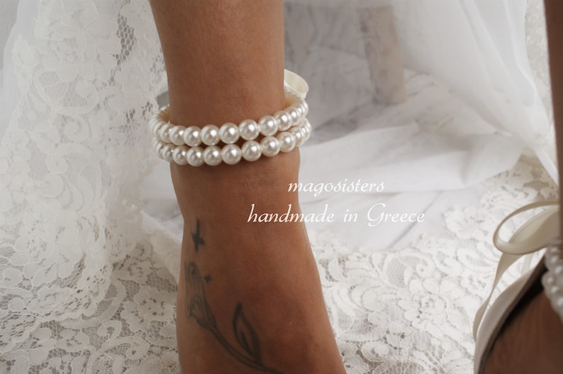 Puede incluir: Un tobillo de perlas blancas con dos filas de perlas. El tobillo est&aacute; en el tobillo de una persona y el texto "magosisters handmade in Greece" es visible debajo del tobillo.