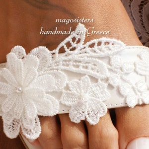 May include: White lace sandals featuring delicate floral designs and pearl accents. The sandals are handmade in Greece by magoosisters.