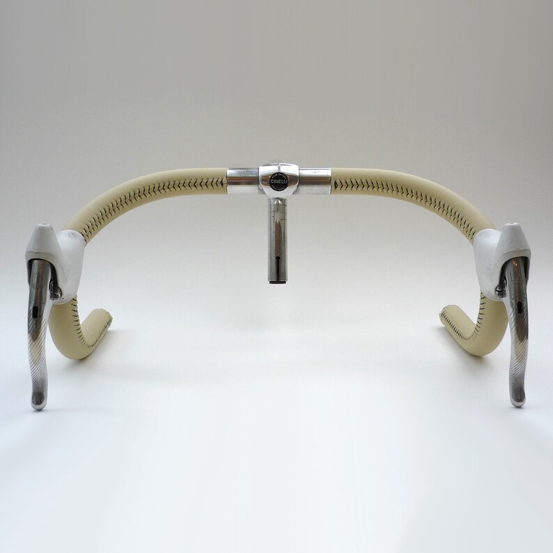 May include: A pair of white leather-wrapped bicycle handlebars with silver brake levers and a silver stem with the word "Cinelli" on it.
