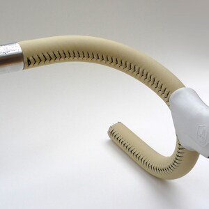 May include: A beige leather handlebar wrap with black stitching. The wrap is designed for a bicycle.