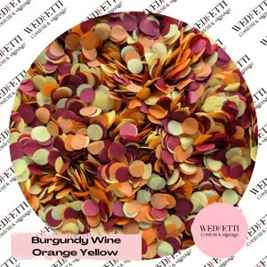 May include: A collection of small, circular paper confetti pieces in a mix of burgundy, orange, and yellow colors. The confetti is displayed in a circular frame with the text WEDFETTI Confetti & signage and Burgundy Wine Orange Yellow.
