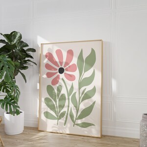 May include: A framed print with a stylized pink flower and green leaves on a white background. The print has a gold frame.