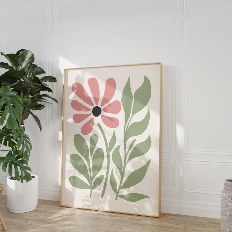May include: A framed print with a stylized pink flower and green leaves on a white background. The print has a gold frame.