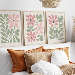 May include: Three framed prints with a minimalist floral design. Each print features pink flowers and green leaves on a cream background.