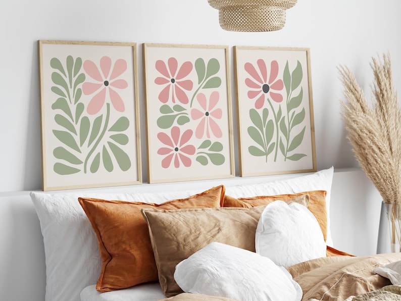 May include: Three framed prints with a minimalist floral design. Each print features pink flowers and green leaves on a cream background.