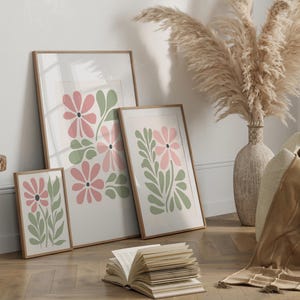 May include: Three framed prints with a floral design. The prints feature pink and green stylized flowers on a white background. The frames are all brown wood.