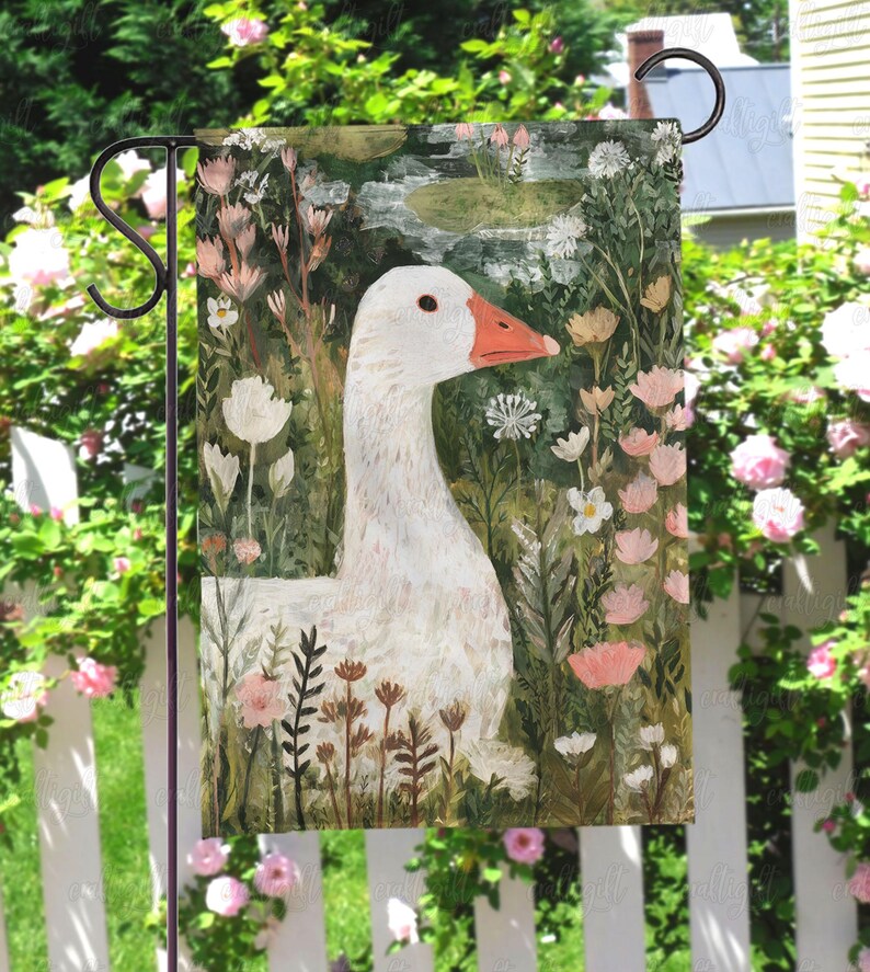 May include: A garden flag featuring a white goose with an orange beak, set against a backdrop of flowers and greenery. The artwork has a painterly style, with soft colors and a whimsical feel. The flag is designed for outdoor use and is displayed on a black metal stand.