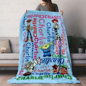 May include: A light blue fleece blanket featuring a grid pattern and the name Charlie repeated in various colors and orientations. The blanket displays cartoon characters including Woody, Jessie, a green alien, Buzz Lightyear, and two potato figures.