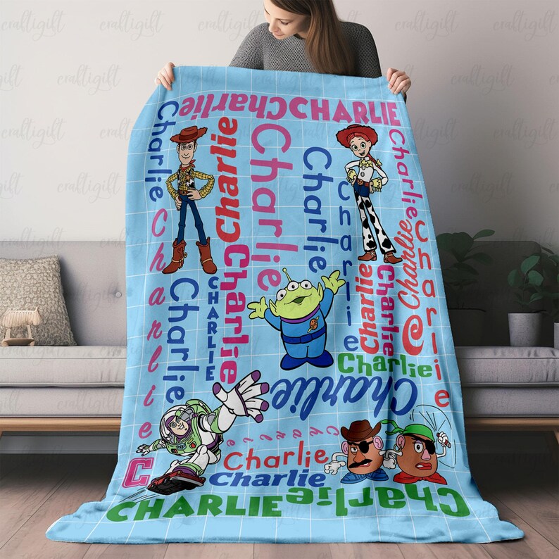 May include: A light blue fleece blanket featuring a grid pattern and the name Charlie repeated in various colors and orientations. The blanket displays cartoon characters including Woody, Jessie, a green alien, Buzz Lightyear, and two potato figures.