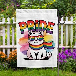 May include: A white garden flag with a cartoon cat wearing rainbow sunglasses and a rainbow scarf. The word "PRIDE" is written in large, colourful letters above the cat. The background has a watercolour rainbow design.