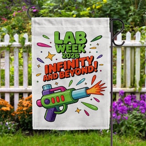 May include: A white garden flag featuring the text "LAB WEEK 2026 INFINITY AND BEYOND!" and a cartoon ray gun illustration. The ray gun is green, purple, and blue, with orange flames. Colourful stars and shapes surround the text and image.