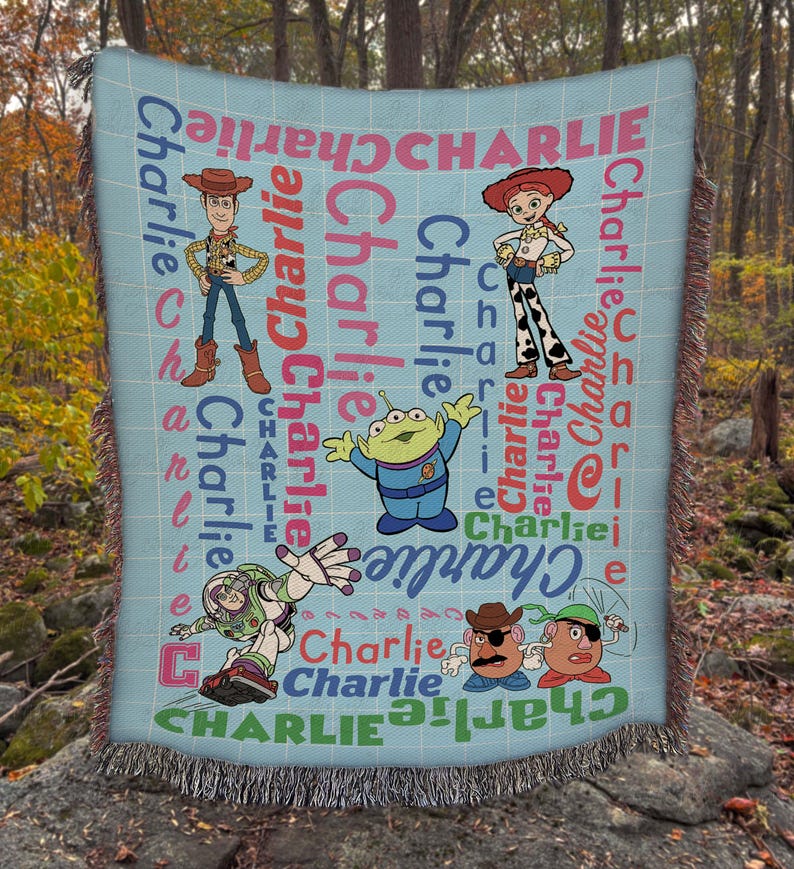 May include: A light blue woven throw blanket featuring Toy Story characters including Woody, Jessie, an alien, Buzz Lightyear, and Mr. and Mrs. Potato Head. The name Charlie is printed repeatedly in various fonts, sizes, and colors across the fabric.