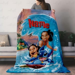 Puede incluir: Una manta azul con personajes de una pel&iacute;cula de animaci&oacute;n popular. La manta tiene un dise&ntilde;o de ola con la palabra "Name" en rojo. Los personajes surfean sobre una ola. El fondo muestra una escena de playa.