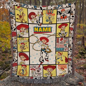 May include: A woven throw blanket featuring a collage of Jessie the Cowgirl from Toy Story in various poses, including lassoing, with the text "NAME", "TIME TO SHINE", "YEEHAW", "COWGIRL AT HEART", and "TOUGH COOKIE" printed on a cream background.