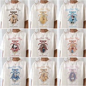 May include: Cream-colored t-shirts with various Disney character designs inside ornate frames. Each shirt features the text "Happiest Mom on Earth" above the character image, including Chip, Pluto, and Minnie Mouse. The designs are in various colors.