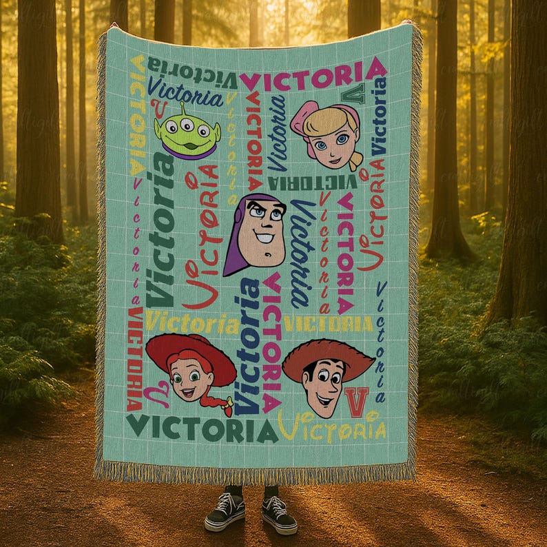 以下が含まれることがあります： グリッドパターンと様々な色やフォントで繰り返される「Victoria」という名前が特徴のライトブルーの織りブランケット。ブランケットには、緑色のエイリアン、金髪の少女、スペースレンジャー、2人のカウボーイなど、漫画のキャラクターの頭部が描かれています。