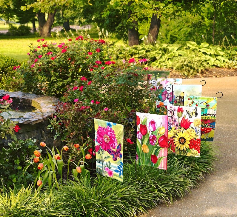 May include: A collection of colorful garden flags with floral and butterfly designs. The flags are displayed on metal poles in a garden setting.