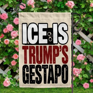 May include: A beige garden flag with the words "ICE IS TRUMP'S GESTAPO" in black, white, and maroon. The word "ICE" is in white block letters, and the word "IS" is in white block letters with handcuffs in the middle. The flag is hanging on a black metal stand.