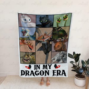 Könnte beinhalten: Eine weiße Decke mit einer Collage aus farbenfrohen Drachenillustrationen. Die Decke trägt den schwarzen Text "IN MY DRAGON ERA". Die Decke wird von einer Person gehalten.