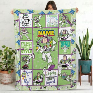 K&ouml;nnte beinhalten: Eine rechteckige Fleecedecke mit einem Gittermuster und mehreren Illustrationen der Figur Buzz Lightyear in verschiedenen Posen. Das Design umfasst gr&uuml;ne, violette und wei&szlig;e Farben mit Texten wie You've got a Friend in Me, I NEED SPACE und NAME.
