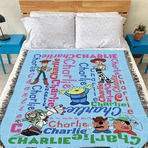 May include: A light blue woven throw blanket featuring a grid pattern and the name Charlie repeated in various colors and fonts. The blanket displays cartoon characters including Woody, Jessie, an alien, Buzz Lightyear, and Mr. Potato Head.