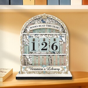 May include: A decorative bookshelf-shaped book counter with the text "BOOKS READ THIS YEAR" and the number "126". The counter has a floral design and the text "Veronica's Library".