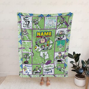 K&ouml;nnte beinhalten: Eine gr&uuml;ne Fleecedecke mit mehreren Feldern, die die Figur Buzz Lightyear in verschiedenen Posen zeigen. Die Decke enth&auml;lt Texte wie You've got a Friend in Me, I NEED SPACE, I'M NOT CLUMSY I'M FALLING WITH STYLE und Reach for infinity and beyond.