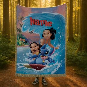 Puede incluir: Una manta tejida con una vibrante ilustraci&oacute;n de personajes de una popular pel&iacute;cula de animaci&oacute;n. El dise&ntilde;o incluye una gran ola, la palabra "Name" en rojo y varios personajes de dibujos animados. La manta tiene un borde con flecos.
