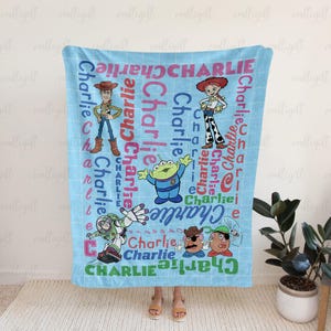 May include: A light blue fleece blanket featuring a grid pattern and the name Charlie repeated in various colors and fonts. The design includes illustrations of Woody, Jessie, Buzz Lightyear, an alien, and Mr. Potato Head from Toy Story.