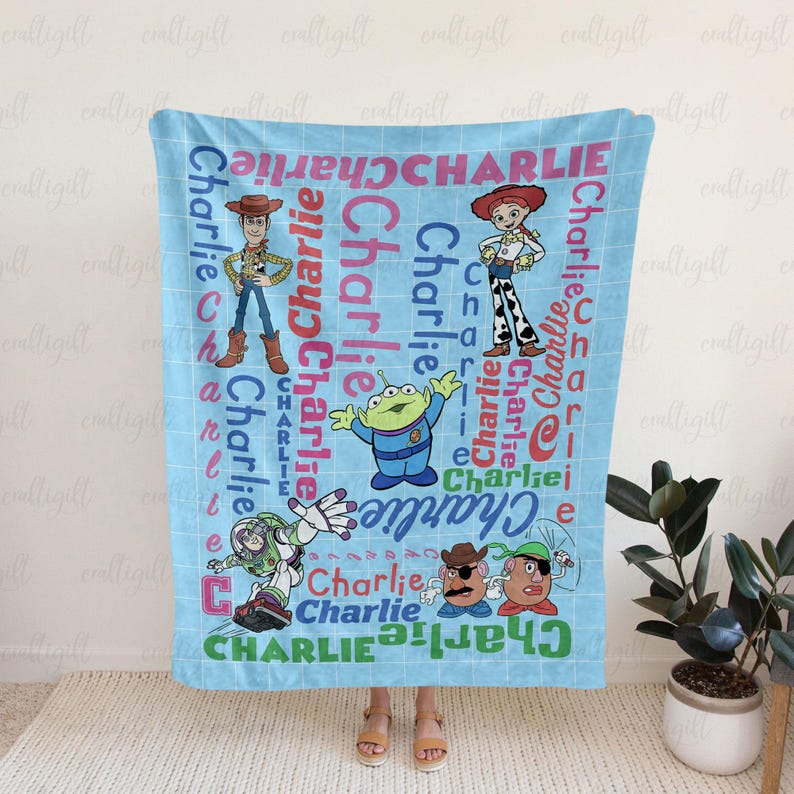 May include: A light blue fleece blanket featuring a grid pattern and the name Charlie repeated in various colors and fonts. The design includes illustrations of Woody, Jessie, Buzz Lightyear, an alien, and Mr. Potato Head from Toy Story.