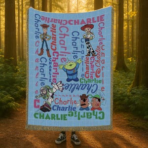 May include: A light blue woven throw blanket featuring a grid pattern and the name Charlie repeated in various colors and fonts. The blanket displays cartoon characters including a cowboy, a cowgirl, a green alien, a space ranger, and two potatoes.