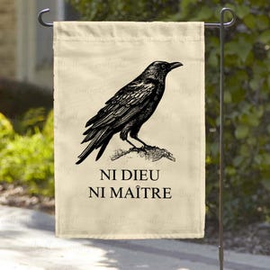 May include: A cream-colored garden flag with a black silhouette of a crow perched on a branch. The flag has the text "Ni Dieu Ni Ma&icirc;tre" printed in black.