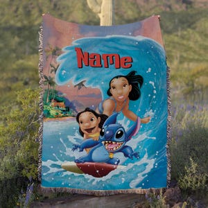 Puede incluir: Una manta tejida con una vibrante ilustraci&oacute;n de Stitch surfeando una ola con dos chicas. La manta tiene una escena oce&aacute;nica azul y blanca con el nombre "Name" en letras rojas. La manta tiene un borde con flecos.