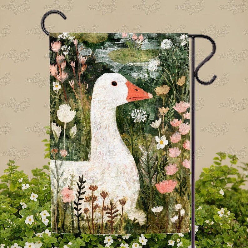 May include: A garden flag featuring a white goose with an orange beak, set amidst a lush garden scene with pink and white flowers. The artwork has a painterly style, with a pond in the background.
