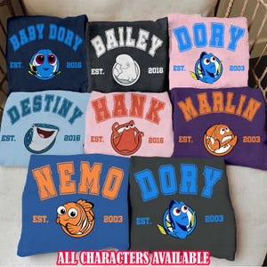 May include: A set of ten colorful sweatshirts featuring different characters from the animated film Finding Nemo. Each sweatshirt has a different character's name and a year of establishment. The characters include Baby Dory, Bailey, Dory, Destiny, Hank, Marlin, Nemo, and Dory.