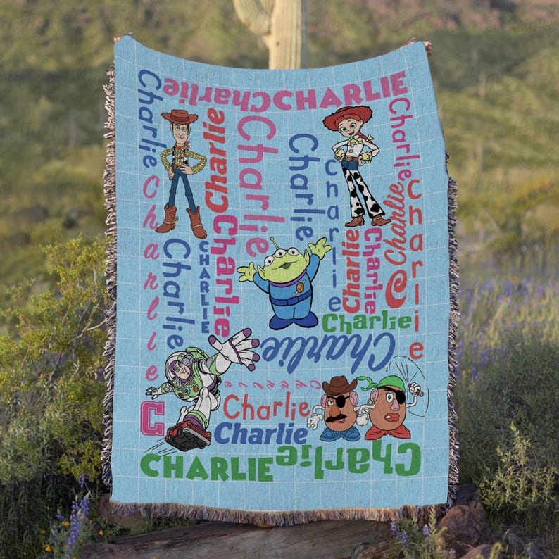 May include: A light blue woven throw blanket featuring the name Charlie repeated in various colors and fonts, alongside illustrations of Toy Story characters including Woody, Jessie, Buzz Lightyear, and Mr. Potato Head with a green alien.