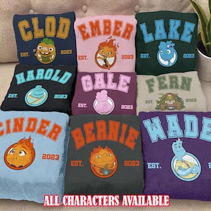 May include: Nine different colored t-shirts with cartoon characters and the text "EST. 2023" on each. The characters include Clod, Ember, Lake, Harold, Gale, Fern, Cinder, Bernie, and Wade. The text "ALL CHARACTERS AVAILABLE" is at the bottom of the image.