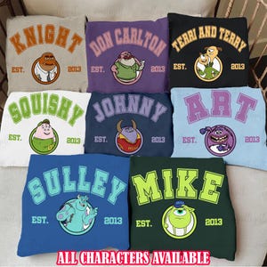 Op de afbeelding: Acht verschillende gekleurde sweatshirts met een college-ontwerp met personages uit de film Monsters Inc. Elk sweatshirt heeft een ander personage en een andere naam, waaronder Sully, Mike, Knight, Don Carlton, Terri en Terry, Squishy, Johnny en Art. De tekst "EST. 2013" staat op elk sweatshirt.