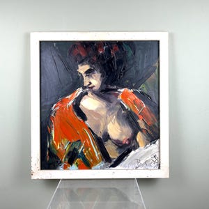 May include: Oil painting of a person in a white frame. The artwork features a figure with dark hair and an orange garment. The painting uses a palette of dark blues, oranges, and skin tones. The style is expressive with visible brushstrokes.