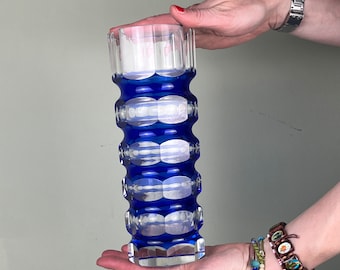 May include: A tall, clear glass vase with a cobalt blue design. The vase has a geometric pattern of alternating blue and clear bands.