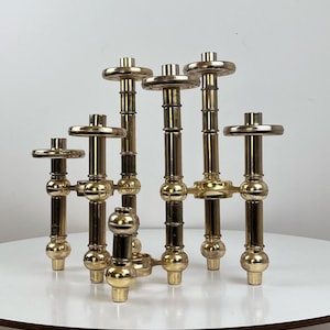 Puede incluir: Un candelabro de latón con seis portavelas. El candelabro está hecho de varias piezas conectadas, creando un diseño geométrico.