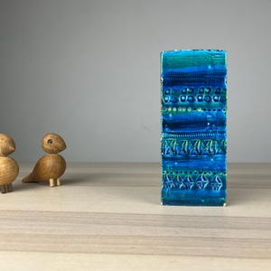 Könnte beinhalten: Eine rechteckige Keramikvase mit strukturierter Oberfläche, in Blau- und Türkistönen und geometrischen Mustern. Links von der Vase befinden sich zwei kleine Holzvögel. Die Vase ist etwa 25 cm hoch.