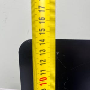 May include: A yellow measuring tape showing a measurement of approximately 25 cm against a black surface. The tape is marked with black numbers and lines, indicating centimeters.