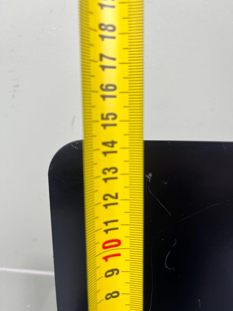 May include: A yellow measuring tape showing a measurement of approximately 25 cm against a black surface. The tape is marked with black numbers and lines, indicating centimeters.