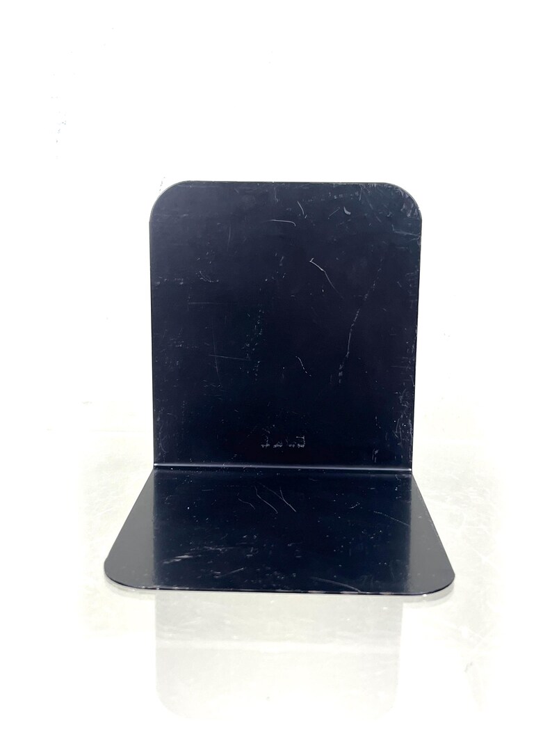 May include: A black metal bookend with a rectangular back and a right-angled base. The bookend has a glossy finish and a few scratches. The word "Luce" is etched on the back. The bookend is designed to hold books upright.