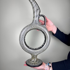 Puede incluir: Una jarra de cerámica negra con un diseño blanco. La jarra tiene una base redonda y un pico largo y curvo. El diseño de la jarra es intrincado y detallado.